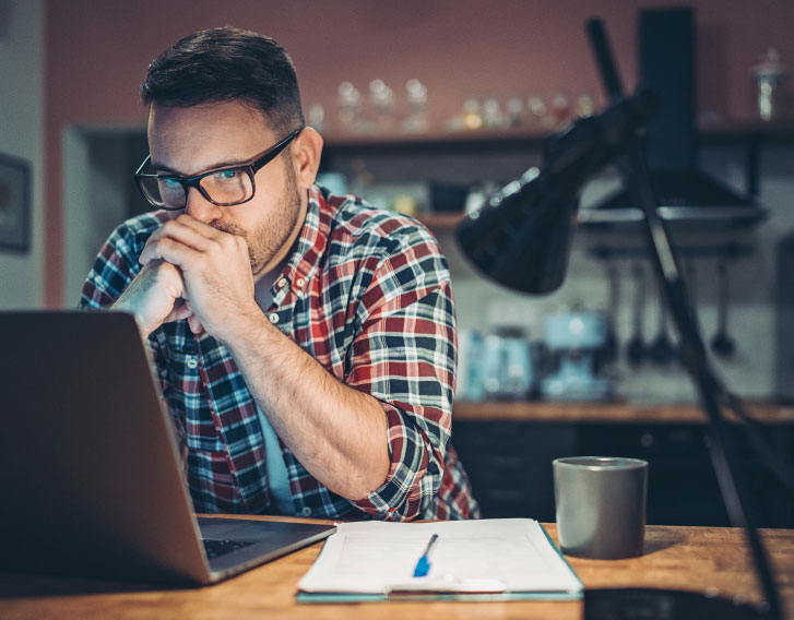 man in deep thought while sitting at a desk with his laptop